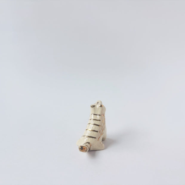 Very small glossy ceramic tiger sculpture, white with gold stripes and golden poppy flower design on its fur. It sits with a cute, happy expression.
