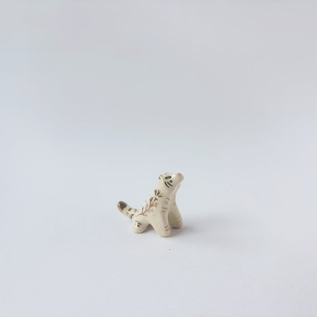 Very small glossy ceramic tiger sculpture, white with gold stripes and golden poppy flower design on its fur. It sits with a cute, happy expression.