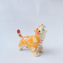 Glossy ceramic sculpture of a tiger with a white underbelly and orange fur with red stripes, gold detailing and white carved poppy flowers. It is in a roaring stance.