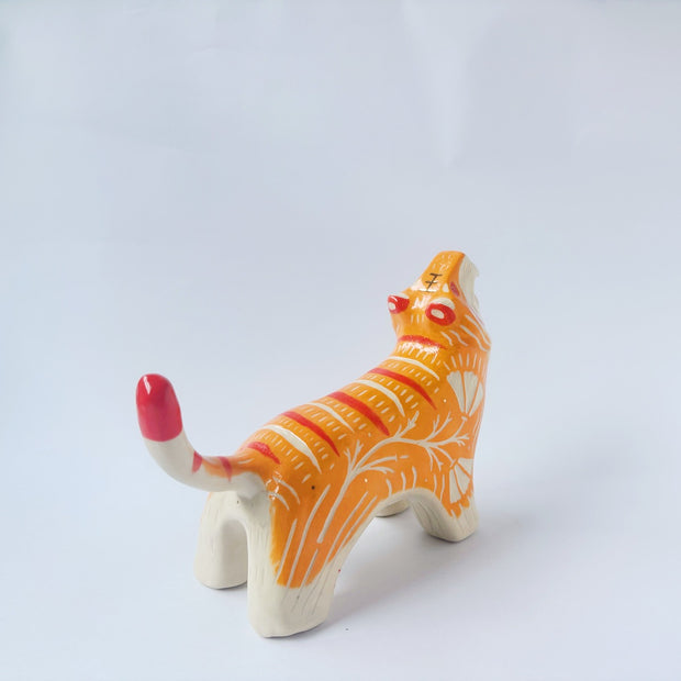 Glossy ceramic sculpture of a tiger with a white underbelly and orange fur with red stripes, gold detailing and white carved poppy flowers. It is in a roaring stance.