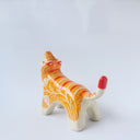 Glossy ceramic sculpture of a tiger with a white underbelly and orange fur with red stripes, gold detailing and white carved poppy flowers. It is in a roaring stance.