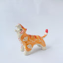 Glossy ceramic sculpture of a tiger with a white underbelly and orange fur with red stripes, gold detailing and white carved poppy flowers. It is in a roaring stance.
