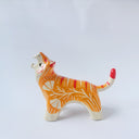 Glossy ceramic sculpture of a tiger with a white underbelly and orange fur with red stripes, gold detailing and white carved poppy flowers. It is in a roaring stance.