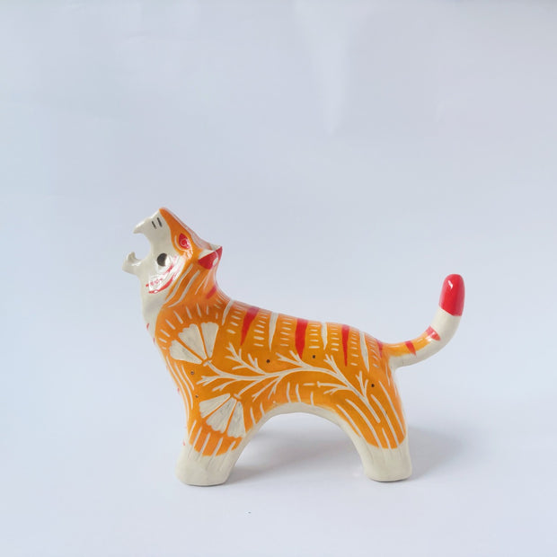 Glossy ceramic sculpture of a tiger with a white underbelly and orange fur with red stripes, gold detailing and white carved poppy flowers. It is in a roaring stance.