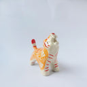 Glossy ceramic sculpture of a tiger with a white underbelly and orange fur with red stripes, gold detailing and white carved poppy flowers. It is in a roaring stance.