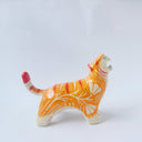 Glossy ceramic sculpture of a tiger with a white underbelly and orange fur with red stripes, gold detailing and white carved poppy flowers. It is in a roaring stance.