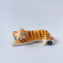 Glossy ceramic sculpture of a tiger, laying down asleep. It has a carved poppy flower pattern and gold detailing.