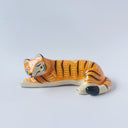Glossy ceramic sculpture of a tiger, laying down asleep. It has a carved poppy flower pattern and gold detailing.