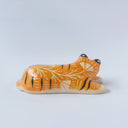 Glossy ceramic sculpture of a tiger, laying down asleep. It has a carved poppy flower pattern and gold detailing.