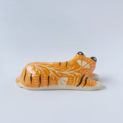 Glossy ceramic sculpture of a tiger, laying down asleep. It has a carved poppy flower pattern and gold detailing.