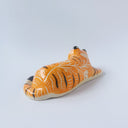 Glossy ceramic sculpture of a tiger, laying down asleep. It has a carved poppy flower pattern and gold detailing.