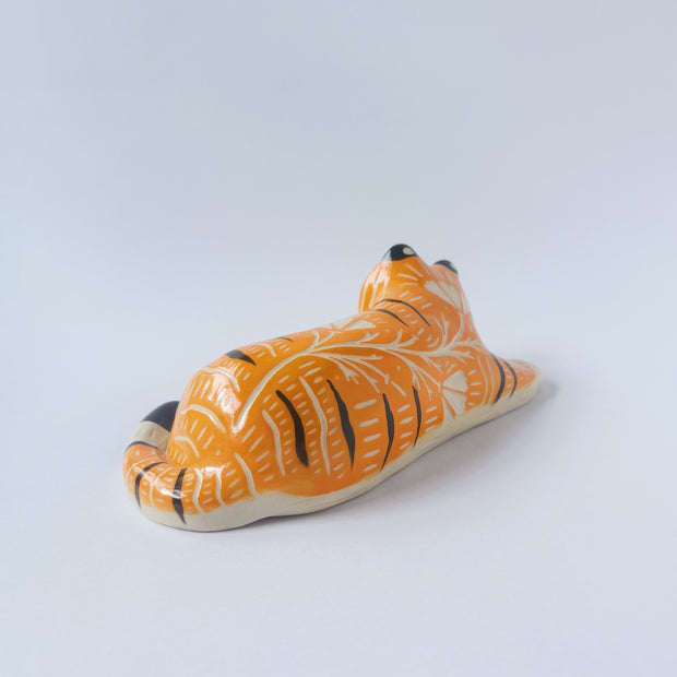 Glossy ceramic sculpture of a tiger, laying down asleep. It has a carved poppy flower pattern and gold detailing.