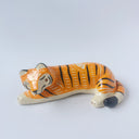 Glossy ceramic sculpture of a tiger, laying down asleep. It has a carved poppy flower pattern and gold detailing.