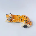 Glossy ceramic sculpture of a tiger, laying down asleep. It has a carved poppy flower pattern and gold detailing.