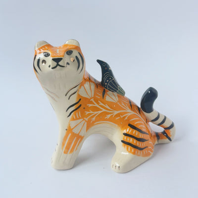 Glossy ceramic sculpture of a lion, sitting with a magpie on its back. The tiger has a carved poppy flower design on its back and gold detailing.