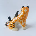 Glossy ceramic sculpture of a lion, sitting with a magpie on its back. The tiger has a carved poppy flower design on its back and gold detailing.