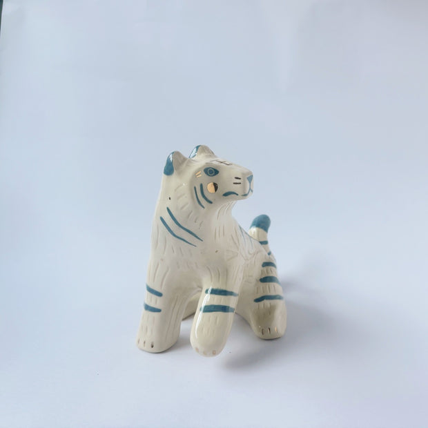 Glossy ceramic sculpture of a white tiger with blue stripes and subtle gold detailing.