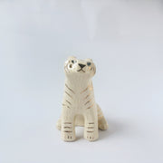 Glossy ceramic tiger sculpture, white with gold stripes and golden poppy flower design on its fur. It sits with a cute, happy expression.
