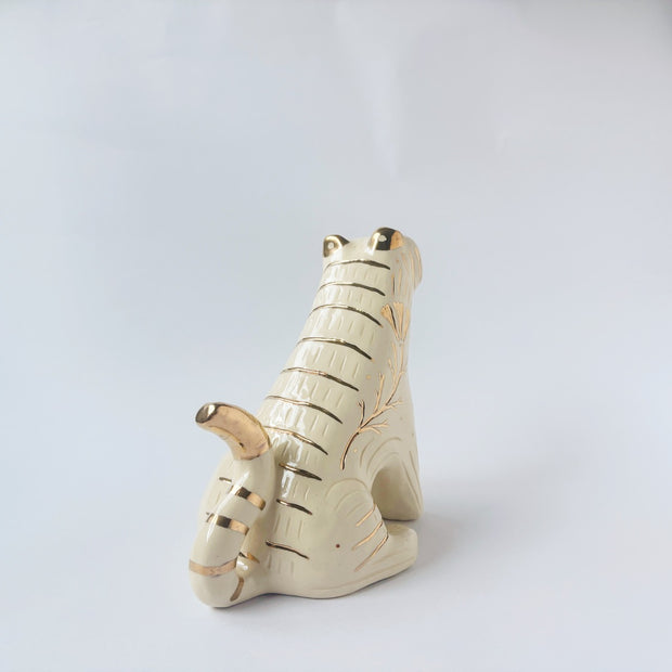 Glossy ceramic tiger sculpture, white with gold stripes and golden poppy flower design on its fur. It sits with a cute, happy expression.