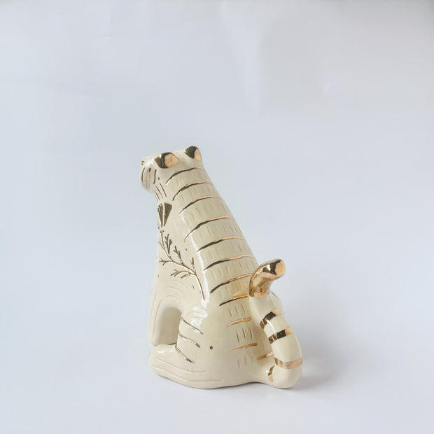 Glossy ceramic tiger sculpture, white with gold stripes and golden poppy flower design on its fur. It sits with a cute, happy expression.