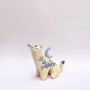 Cream colored ceramic sculpture of a wolf, with a blue crescent moon on its back and floral blue artwork on its body.