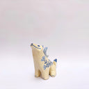 Cream colored ceramic sculpture of a wolf, with a blue crescent moon on its back and floral blue artwork on its body.