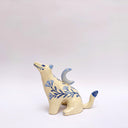 Cream colored ceramic sculpture of a wolf, with a blue crescent moon on its back and floral blue artwork on its body.