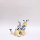 Cream colored ceramic sculpture of a wolf, with a blue crescent moon on its back and floral blue artwork on its body.