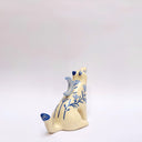 Cream colored ceramic sculpture of a wolf, with a blue crescent moon on its back and floral blue artwork on its body.