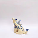 Cream colored ceramic sculpture of a wolf, with a blue crescent moon on its back and floral blue artwork on its body.