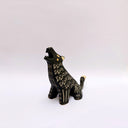 A black ceramic sculpture of a howling wolf with gold painted details and cream colored sgraffito fur details, set against a plain white background.