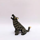 A black ceramic sculpture of a howling wolf with gold painted details and cream colored sgraffito fur details, set against a plain white background.