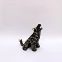 A black ceramic sculpture of a howling wolf with gold painted details and cream colored sgraffito fur details, set against a plain white background.