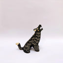 A black ceramic sculpture of a howling wolf with gold painted details and cream colored sgraffito fur details, set against a plain white background.