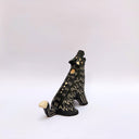 A black ceramic sculpture of a howling wolf with gold painted details and cream colored sgraffito fur details, set against a plain white background.