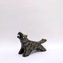 A black ceramic wolf figurine with cream colored sgraffito fur texture, it has 2 tails and howls upwards, with an open mouth.