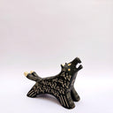 A black ceramic wolf figurine with cream colored sgraffito fur texture, it has 2 tails and howls upwards, with an open mouth.