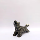 A black ceramic wolf figurine with cream colored sgraffito fur texture, it has 2 tails and howls upwards, with an open mouth.