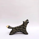 A black ceramic wolf figurine with cream colored sgraffito fur texture, it has 2 tails and howls upwards, with an open mouth.