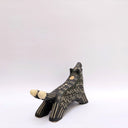 A black ceramic wolf figurine with cream colored sgraffito fur texture, it has 2 tails and howls upwards, with an open mouth.