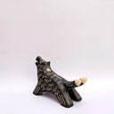 A black ceramic wolf figurine with cream colored sgraffito fur texture, it has 2 tails and howls upwards, with an open mouth.
