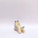 Cream colored ceramic sculpture of a wolf with a small cream colored frog on its back. Both have blue colored floral design motifs on the sides of their bodies. The wolf holds a dark blue tassel in its mouth.