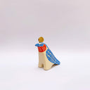 A ceramic bird sculpture with a natural cream colored clay body, blue wings and face detailing, red neck feathers, and a gold circular topper on its head, photographed on a clean light gray studio background.