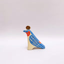 A ceramic bird sculpture with a natural cream colored clay body, blue wings and face detailing, red neck feathers, and a gold circular topper on its head, photographed on a clean light gray studio background.