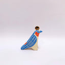 A ceramic bird sculpture with a natural cream colored clay body, blue wings and face detailing, red neck feathers, and a gold circular topper on its head, photographed on a clean light gray studio background.
