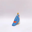 A ceramic bird sculpture with a natural cream colored clay body, blue wings and face detailing, red neck feathers, and a gold circular topper on its head, photographed on a clean light gray studio background.