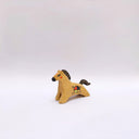 A small ceramic horse figurine in its natural brown clay coloring, decorated with black painted stripes on its mane and tail, and a circular multicolor emblem on its side, set against a plain light gray background.
