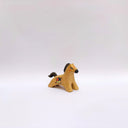 A small ceramic horse figurine in its natural brown clay coloring, decorated with black painted stripes on its mane and tail, and a circular multicolor emblem on its side, set against a plain light gray background.