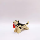 Black and cream colored ceramic sculpture of a husky dog, with a dog pack illustration on the side of its body. It holds a red tassel in its mouth with a small bronze bell.