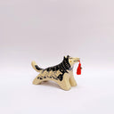 Black and cream colored ceramic sculpture of a husky dog, with a dog pack illustration on the side of its body. It holds a red tassel in its mouth with a small bronze bell.